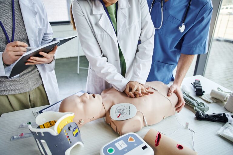 The image shows three individuals, likely medical professionals, practicing CPR on a medical training mannequin