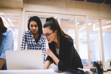 Two women are working together at a desk in a modern office setting.