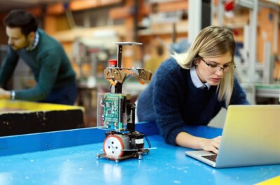 Young beautiful female engineer testing and programming robot